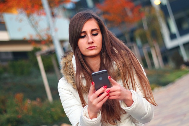 En kvinna med vit jacka och långt brunt hår håller i och tittar på sin smartphone.