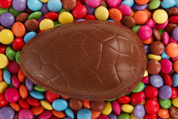 Ett stort chokladägg ligger på en bädd av färgglada chokladlinser.