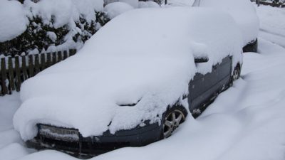 En bil står intill ett staket. Bilen är helt översnöad. Det syns bara däcken och en bit längst ner på bilen.