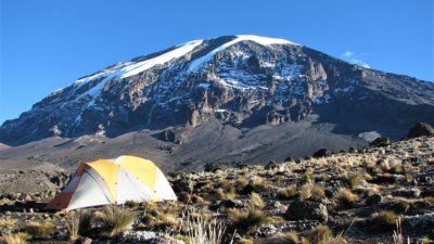 Berget Kilimanjaro är i bakgrunden. Framför Kilimanjaro är ett gult tält på en gräsplätt.