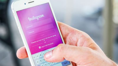 Bild på en hand som håller i en mobil. På displayen syns Instagrams förstasida.