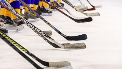Bild på ett hockeylag som tackar motståndarna efter en match. De står med sina hockeklubbor lutade mot isen.