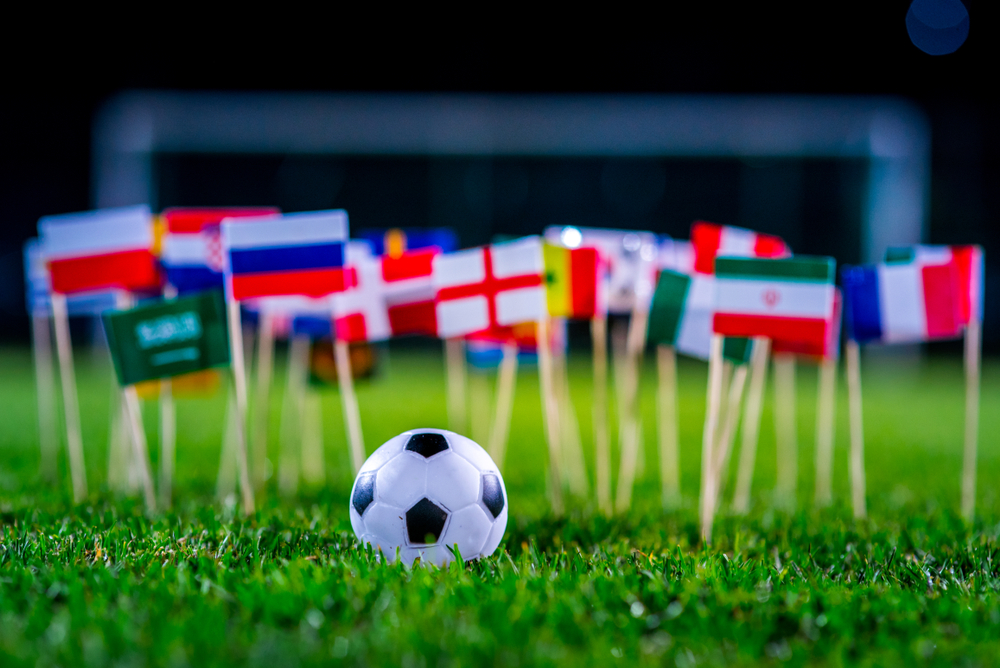 Massa små flaggor på pinnar är nedstuckna i gräset på en fotbollsplan. Framför dem ligger en liten fotboll.