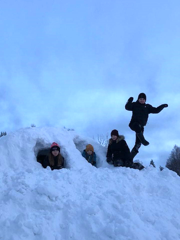 En stor snöhög med fyra elever som tittar fram ur gångarna i den.